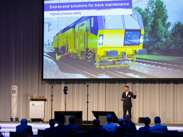 O dr. Florian Auer discursando sobre os próximos desenvolvimentos previstos para as máquinas autônomas de construção ferroviária.